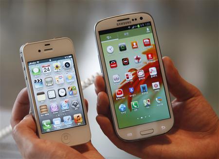 File photo of an employee holding Apple's iPhone 4s and Samsung's Galaxy S III at a store in Seoul