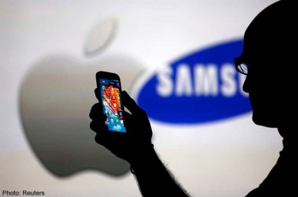 A man is silhouetted against a video screen with Apple and Samsung logos as he poses with a Samsung Galaxy S4 in this photo illustration taken in the central Bosnian town of Zenica