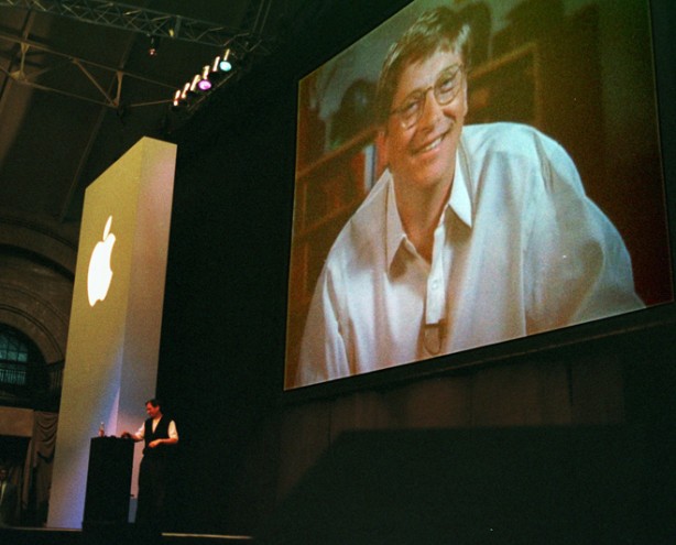 FILE - In this Aug. 6, 1997, file photo, Apple co-founder Steve Jobs, background left, stands at a podium as Bill Gates, chief executive of Microsoft Corp., appears on a video screen during Jobs' address during the MacWorld convention in Boston. Apple Inc. said Jobs died Wednesday. He was 56. (AP Photo/Julia Malakie, File)